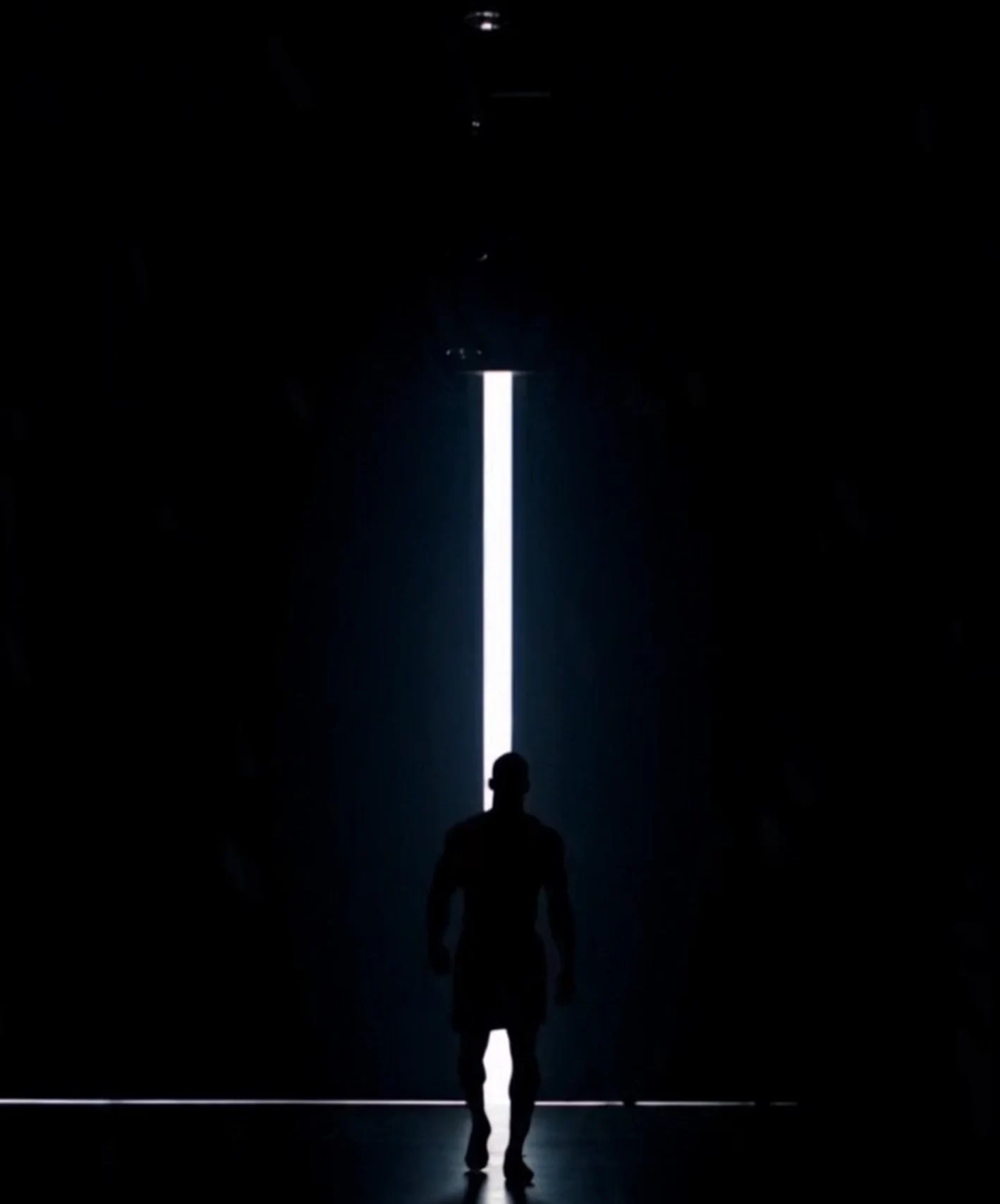 Silhouette of a footballer entering a narrow shaft of stadium light